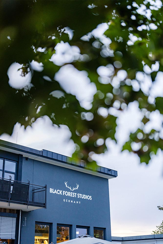 Das moderne Gebäude der Black Forest Studios, teils verdeckt von unscharfen grünen Blättern im Vordergrund.