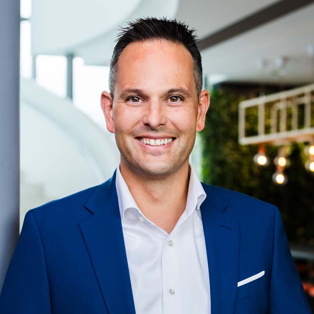 Hans-Martin Hellebrand hat kurz geschnittene, dunkle Haare und trägt ein helles Shirt und ein blaues Sakko, sieht lächelnd in die Kamera.