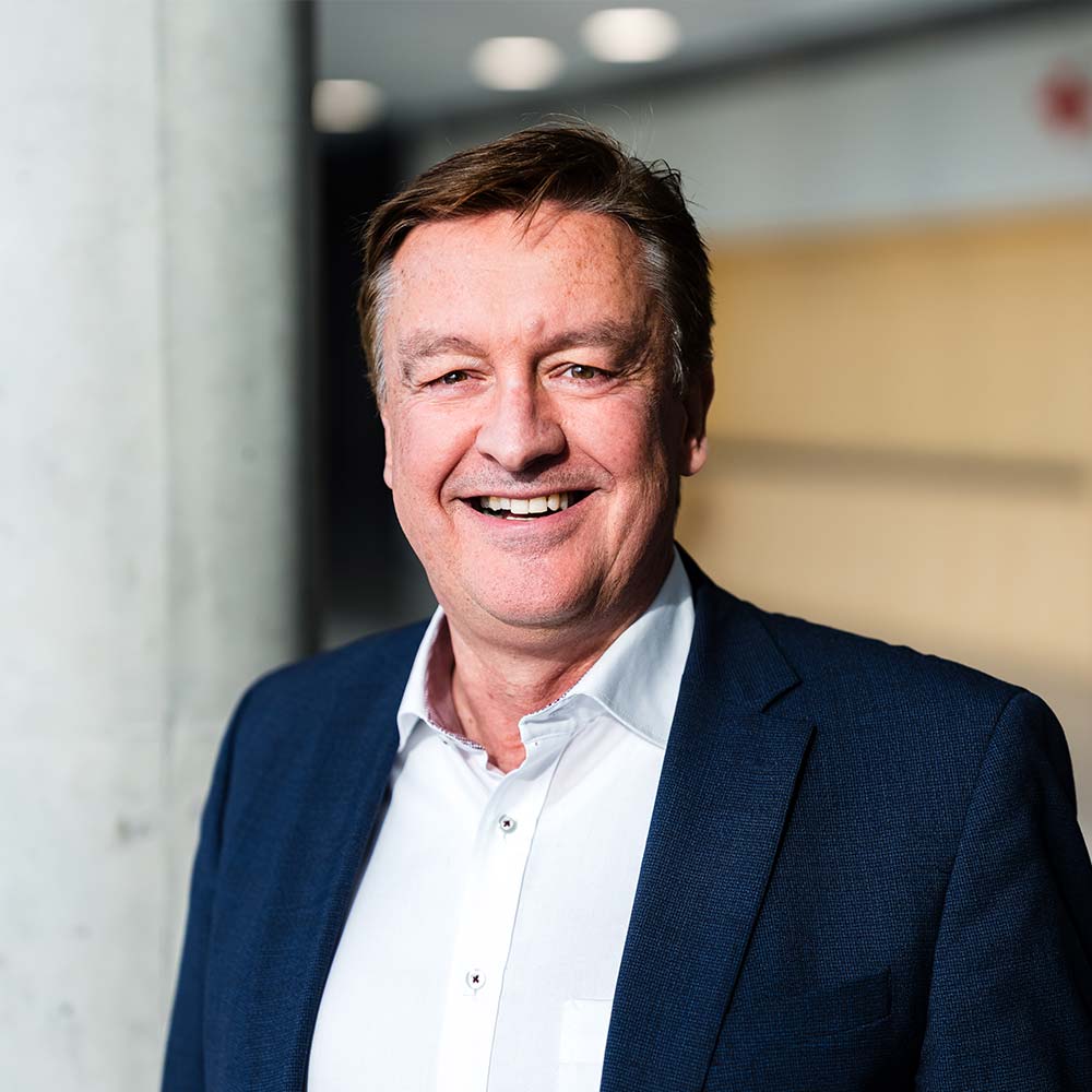 Hans-Jürgen Hamburger, Leiter Systemlösungen Wärme & Erzeugungen: Mann mit braunen Haaren in blauem Anzug lacht in die Kamera