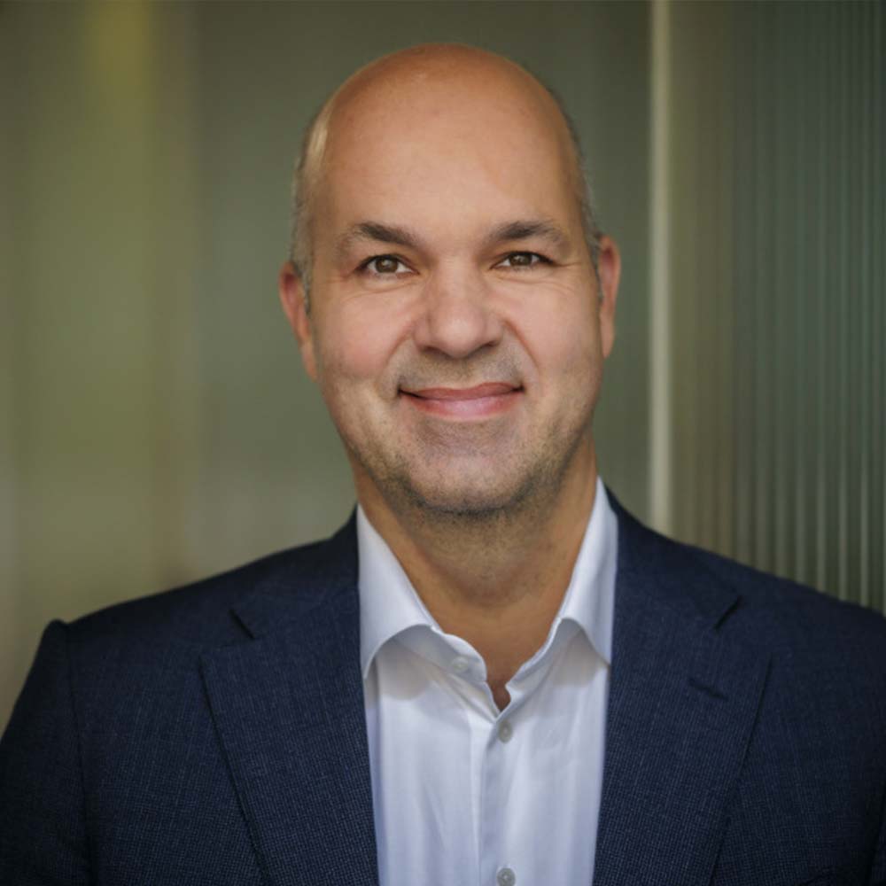 Dr. Marcel Fratzscher trägt ein dunkelblaues Sakko und ein weißes Hemd und schaut freundlich in die Kamera.